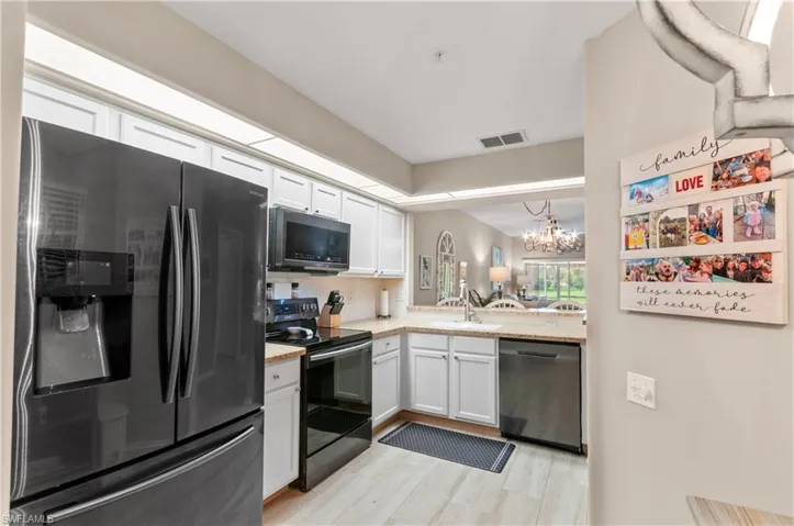 Kitchen with black range with electric stovetop, a sink, white cabinets, stainless steel dishwasher, and freestanding refrigerator