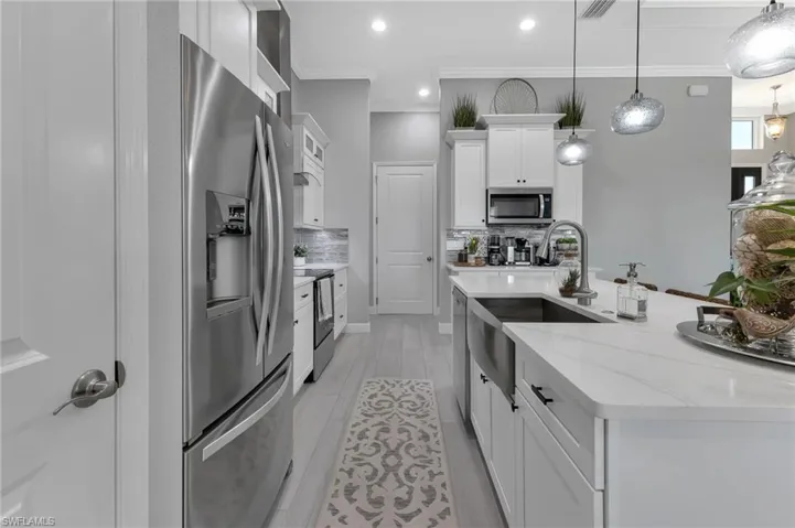 Kitchen with appliances with stainless steel finishes, white cabinetry, backsplash, hanging light fixtures, and light stone countertops