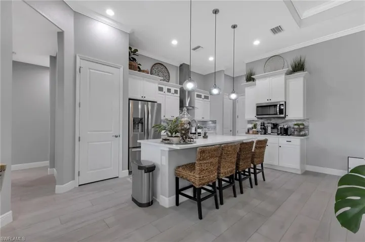 Kitchen featuring hanging light fixtures, a center island with sink, stainless steel appliances, a kitchen bar, and decorative backsplash