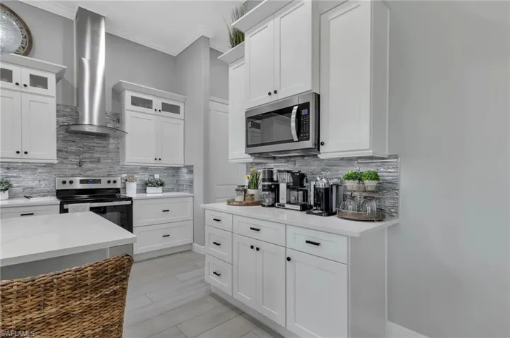 Kitchen with tasteful backsplash, appliances with stainless steel finishes, wall chimney range hood, and white cabinets
