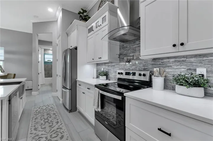Kitchen featuring wall chimney exhaust hood, tasteful backsplash, stainless steel appliances, light stone countertops, and white cabinets