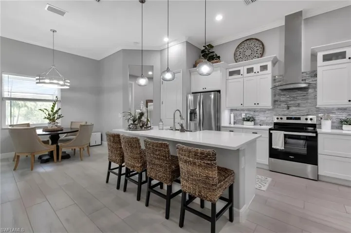 Kitchen with pendant lighting, wall chimney range hood, appliances with stainless steel finishes, a kitchen island with sink, and a kitchen bar