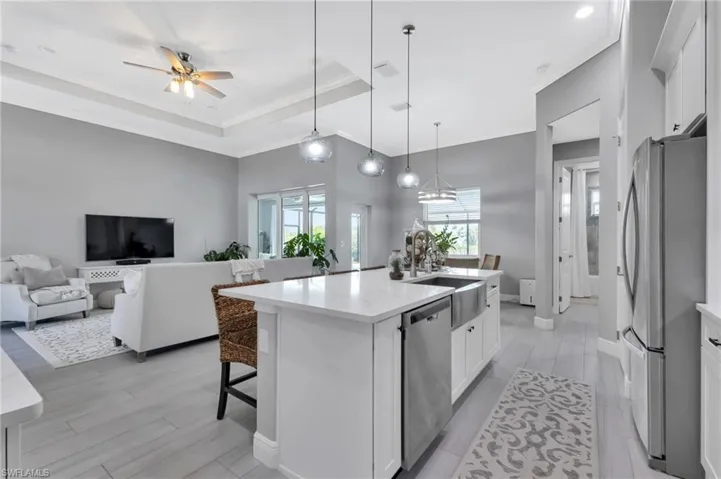 Kitchen featuring stainless steel appliances, decorative light fixtures, a center island with sink, and white cabinets