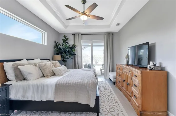 Bedroom featuring multiple windows, access to outside, ceiling fan, and a tray ceiling