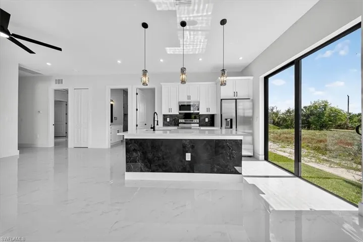 Kitchen with hanging light fixtures, a kitchen island with sink, stainless steel appliances, white cabinets, and decorative backsplash