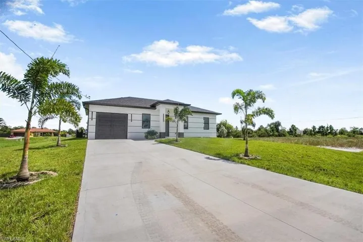 View of front of property with an attached garage, concrete driveway, a front yard, and stucco siding