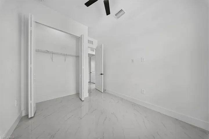 Unfurnished bedroom featuring a closet, light marble finish floors, and ceiling fan