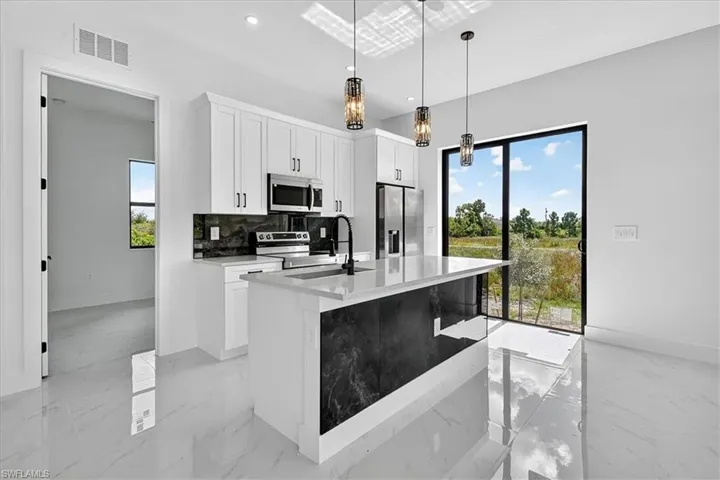 Kitchen featuring light stone countertops, white cabinets, backsplash, stainless steel appliances, and an island with sink