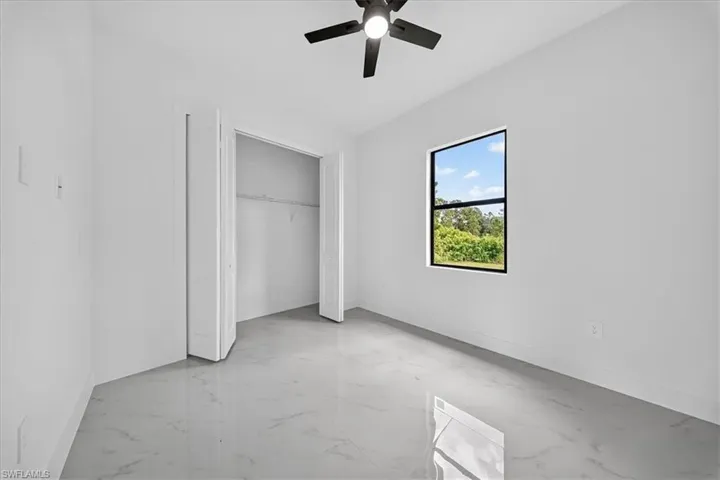 Unfurnished bedroom with light marble finish floors, ceiling fan, and a closet