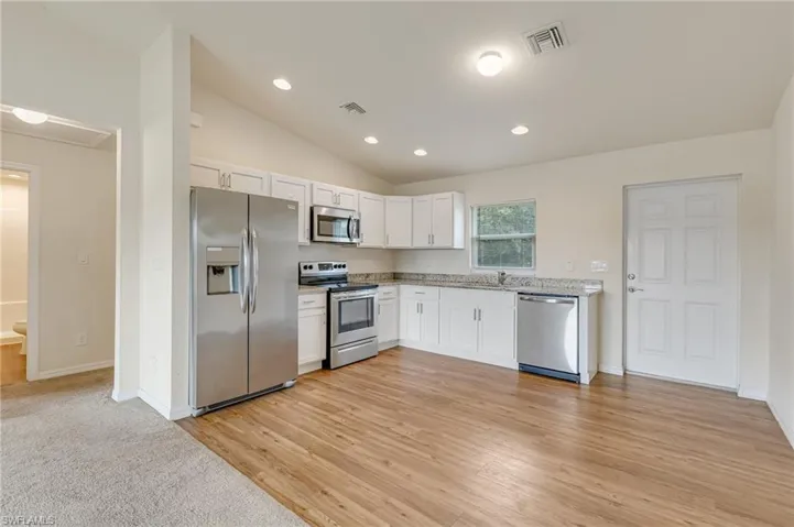 Kitchen with stainless steel appliances, white cabinets, lofted ceiling, light wood finished floors, and light stone counters