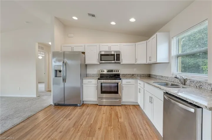 Kitchen with appliances with stainless steel appliances, high ceilings, white sleek cabinetry, light granite countertops, and elegant laminate flooring!