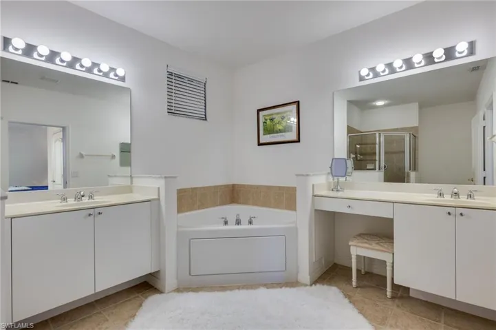 Bathroom featuring two vanities, light tile patterned flooring, a bath, and a stall shower