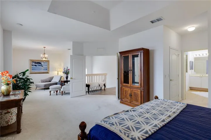 Bedroom with light carpet, suspended lighting, and connected bathroom