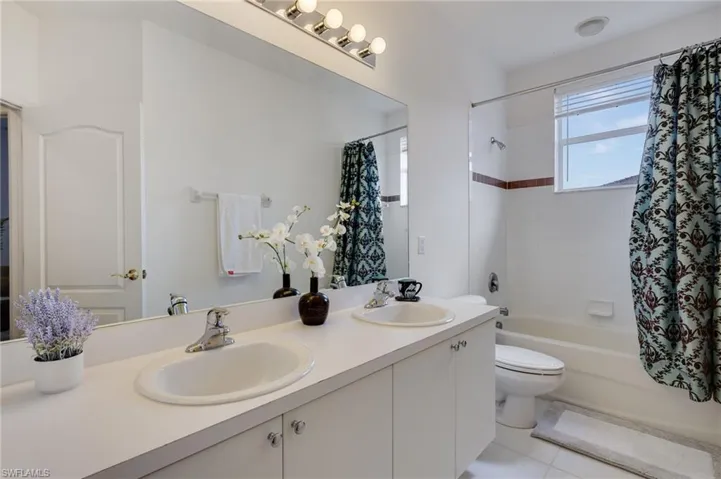Bathroom with double vanity, shower / bathtub combination with curtain, and light tile patterned flooring
