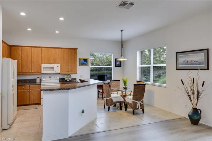 Kitchen featuring white appliances, light tile patterned floors, decorative light fixtures, wood finish cabinetry