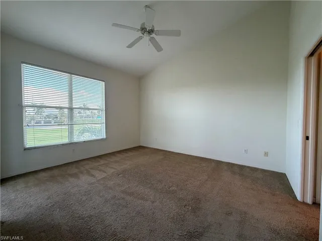 Carpeted spare room with ceiling fan and high vaulted ceiling