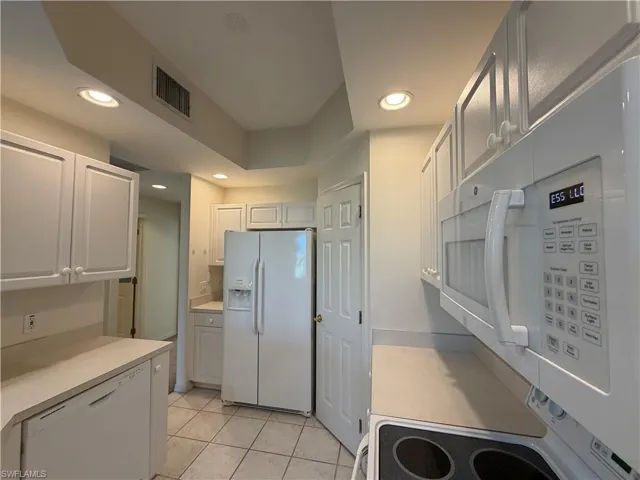 Kitchen with white appliances, light countertops, light tile patterned floors, recessed lighting, and white cabinets