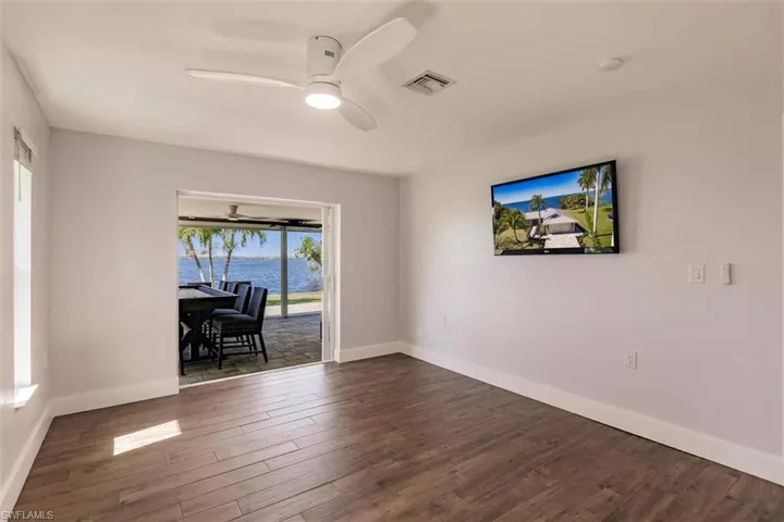 Empty room with a ceiling fan, baseboards, visible vents, and dark wood-type flooring