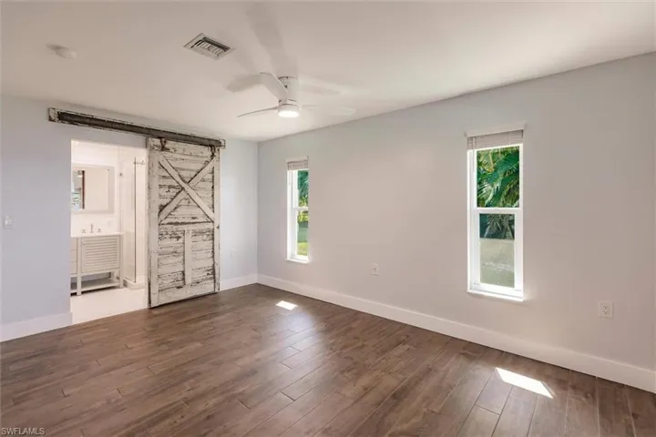 Spare room featuring a barn door, dark wood-type flooring, a ceiling fan, and baseboards