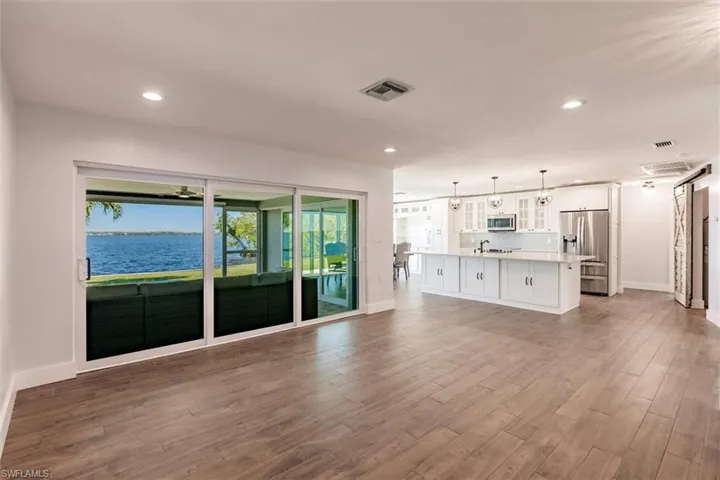Unfurnished living room featuring baseboards, visible vents, dark wood-type flooring, a water view, and recessed lighting