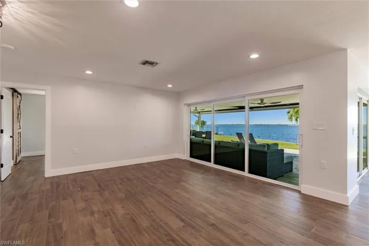 Empty room featuring a water view, visible vents, dark wood finished floors, and recessed lighting