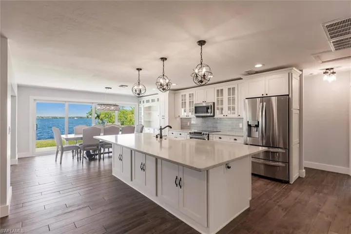 Kitchen featuring appliances with stainless steel finishes, glass insert cabinets, a water view, a kitchen island with sink, and light countertops