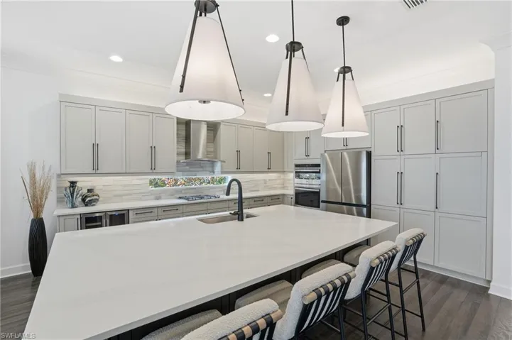 Kitchen featuring dark wood finished floors, a kitchen bar, a kitchen island with sink, decorative light fixtures, and wall chimney range hood