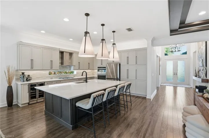 Kitchen featuring a kitchen bar, hanging light fixtures, wine cooler, an island with sink, and recessed lighting