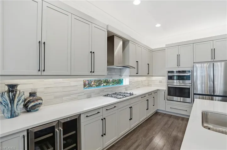 Kitchen featuring stainless steel appliances, wine cooler, wall chimney range hood, dark wood-style floors, and light stone countertops