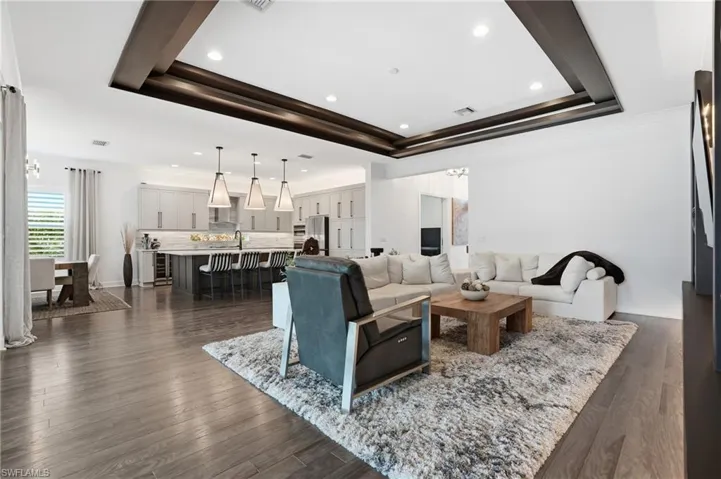 Living room with dark wood-type flooring, ornamental molding, recessed lighting, a tray ceiling, and wine cooler
