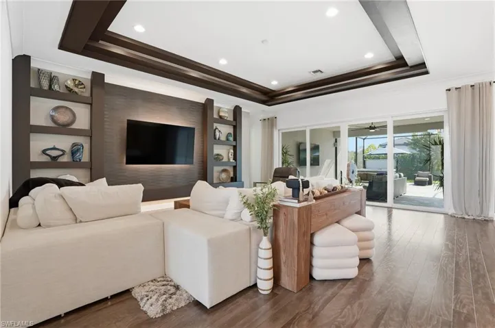 Living room with built in shelves, wood finished floors, a raised ceiling, recessed lighting, and ornamental molding