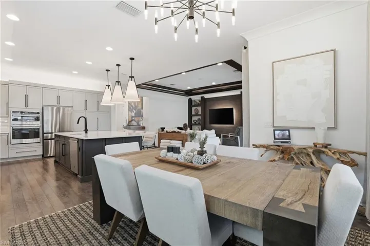 Dining space featuring a tray ceiling, ornamental molding, recessed lighting, dark wood-type flooring, and a chandelier