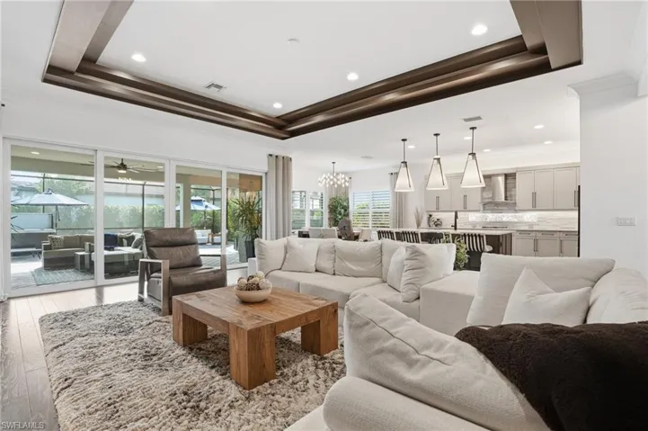 Living room with crown molding, a chandelier, wood-type flooring, a tray ceiling, and recessed lighting
