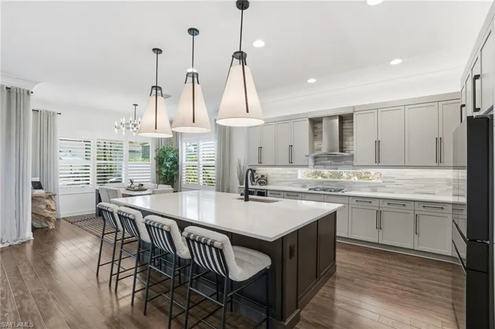 Kitchen featuring a breakfast bar, decorative light fixtures, decorative backsplash, a kitchen island with sink, and crown molding