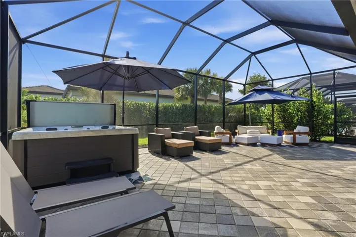 View of patio featuring glass enclosure, a sunroom, outdoor lounge area, and a hot tub