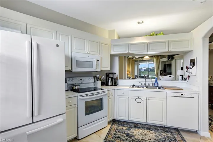 Kitchen featuring white appliances, white cabinetry, light tile patterned floors, and sink
