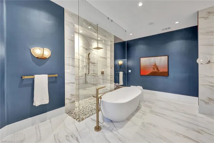 Primary en suite bathroom with frameless double entry shower, spray bar, waterfall shower head, and gorgeous freestanding soaking tub with lovely gold finishes.