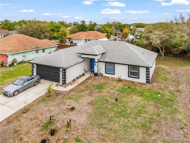 View of front of house featuring an attached garage, concrete driveway, roof with shingles, stucco siding, and view of wooded area