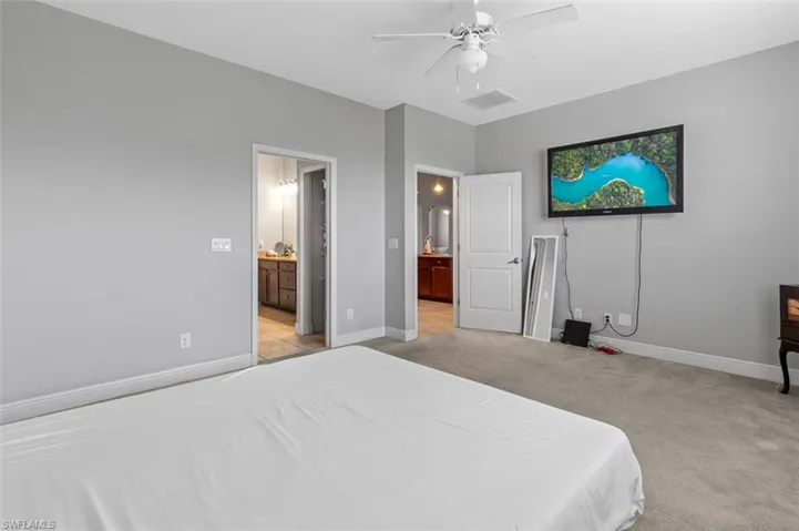 Bedroom featuring light carpet, ensuite bathroom, and ceiling fan