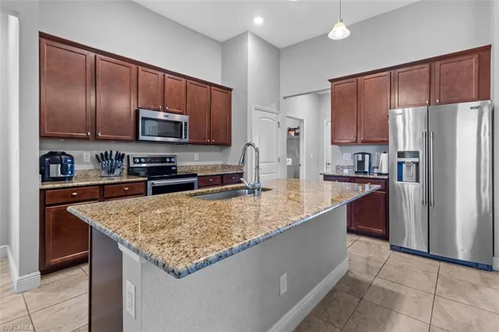 Kitchen featuring hanging light fixtures, a center island with sink, appliances with stainless steel finishes, sink, and light tile floors