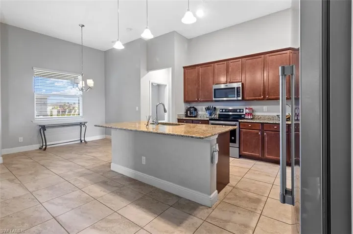 Kitchen featuring hanging light fixtures, stainless steel appliances, a kitchen island with sink, sink, and light tile floors