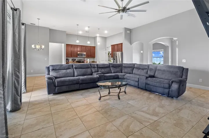 Tiled living room with ceiling fan with notable chandelier and a towering ceiling