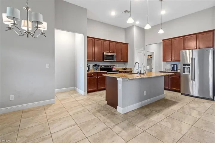 Kitchen with decorative light fixtures, light stone counters, stainless steel appliances, a kitchen island with sink, and a high ceiling
