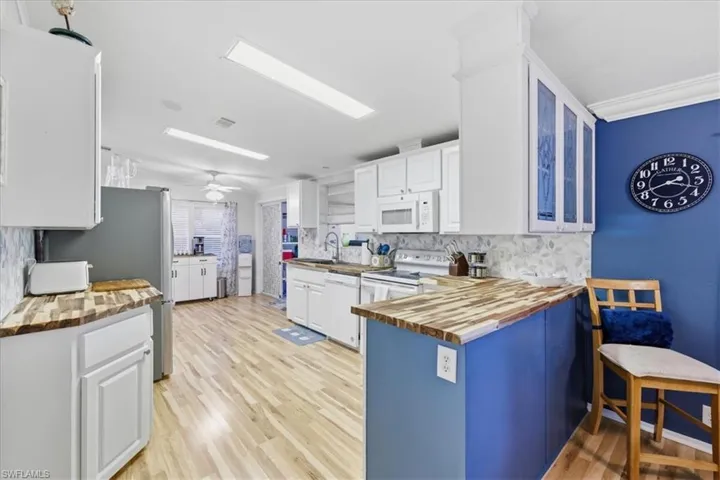 Kitchen featuring white cabinets, wood counters, white appliances, a peninsula, and light wood-style flooring
