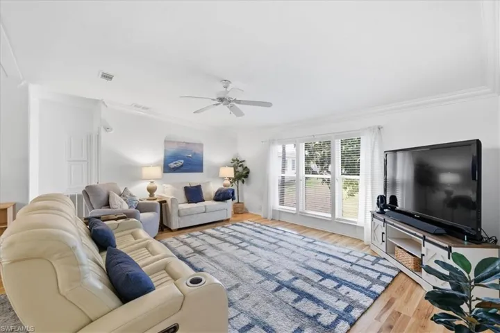 Living room featuring ornamental molding, light wood-type flooring, and a ceiling fan