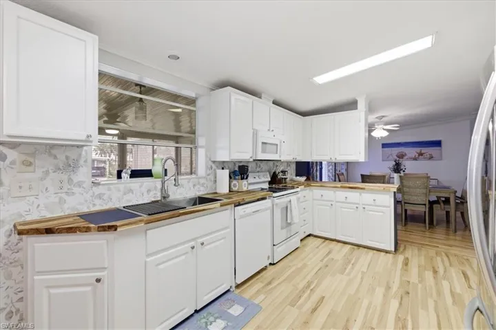 Kitchen featuring a ceiling fan, white appliances, light wood-style flooring, white cabinets, and crown molding