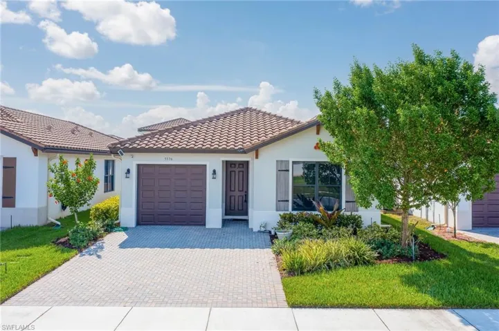 Mediterranean / spanish home with a garage, decorative driveway, a tiled roof, stucco siding, and a front yard