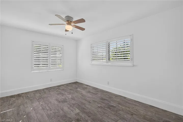 White walls, wood-finish flooring, two windows with plantation shutters, and a ceiling fan with integrated lighting