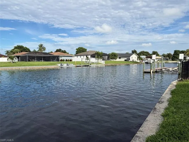 Waterfront property featuring a private boat dock, concrete seawall, and manicured lawn