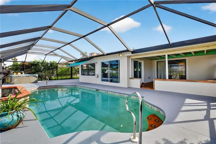 Screened pool enclosure with a curved swimming pool, integrated spa, and an expansive concrete patio